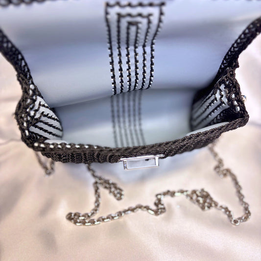 Close-up of a black purse with a silver clasp on a satin fabric background.