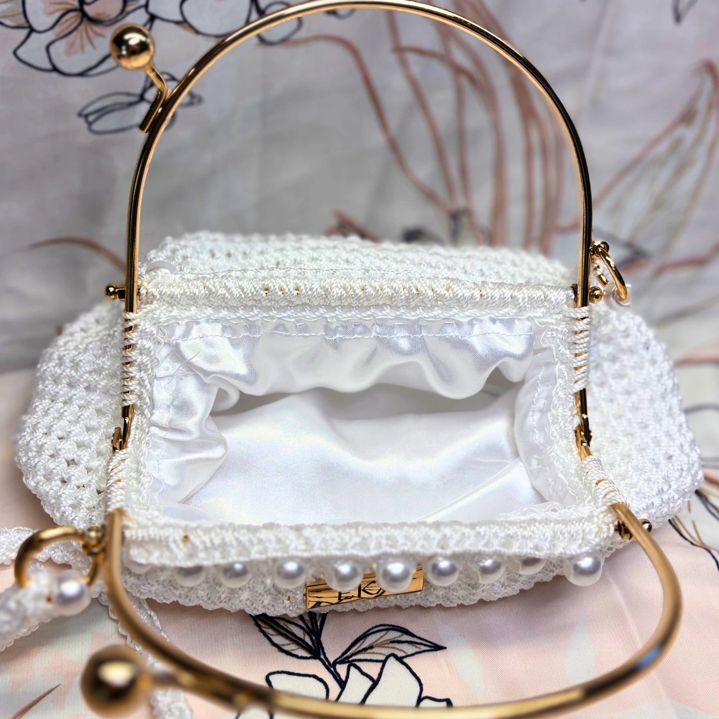 White handbag with gold handle and pearl embellishments on a floral background