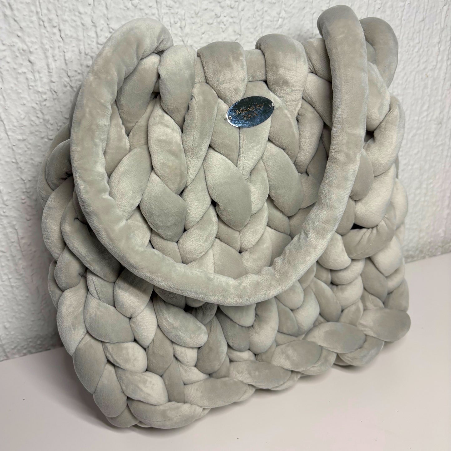 Gray braided bag on a white surface with a textured white wall background