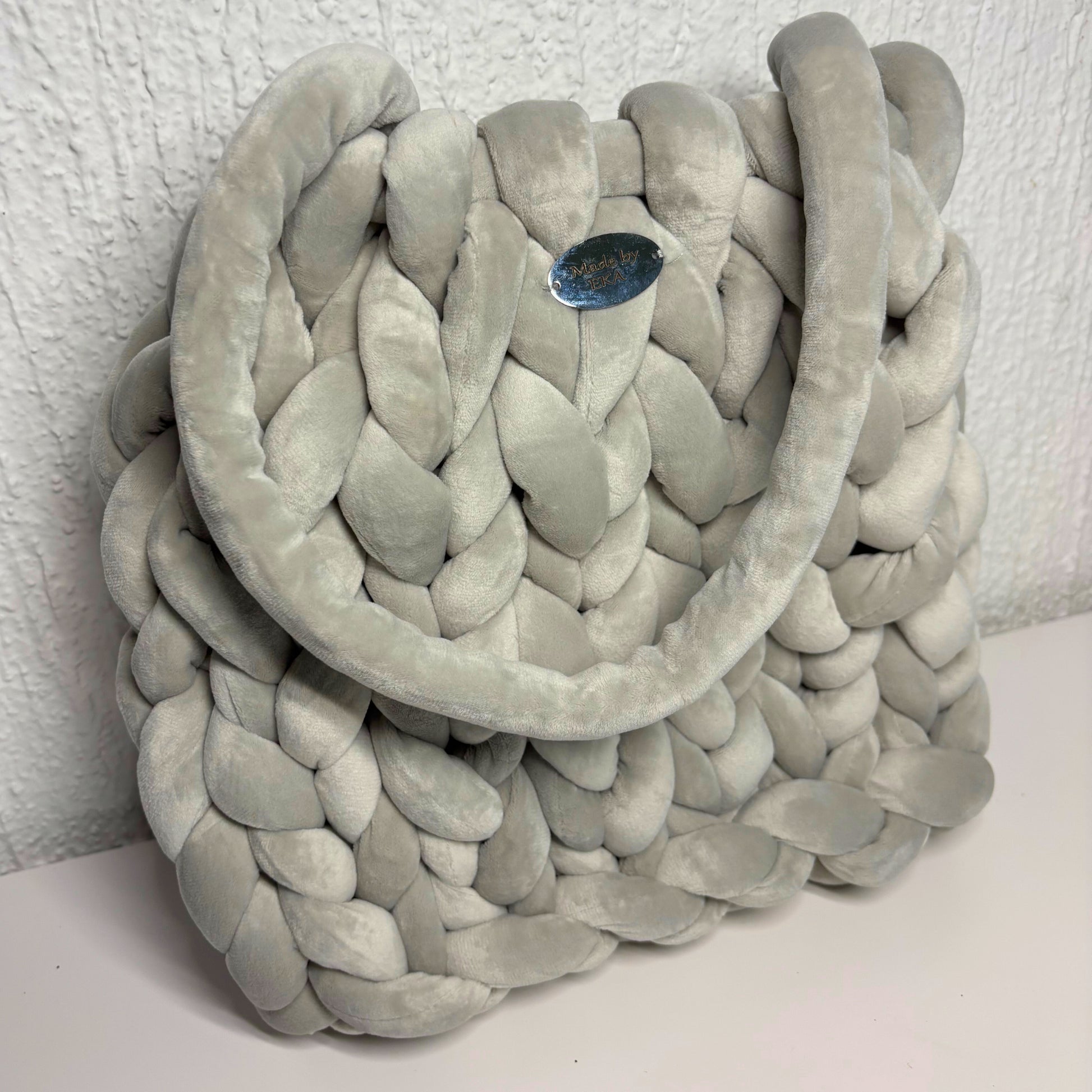 Gray braided bag on a white surface with a textured white wall background