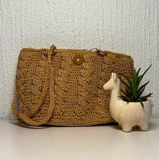 Gold crochet bag with a wooden llama figure and plant on a light background