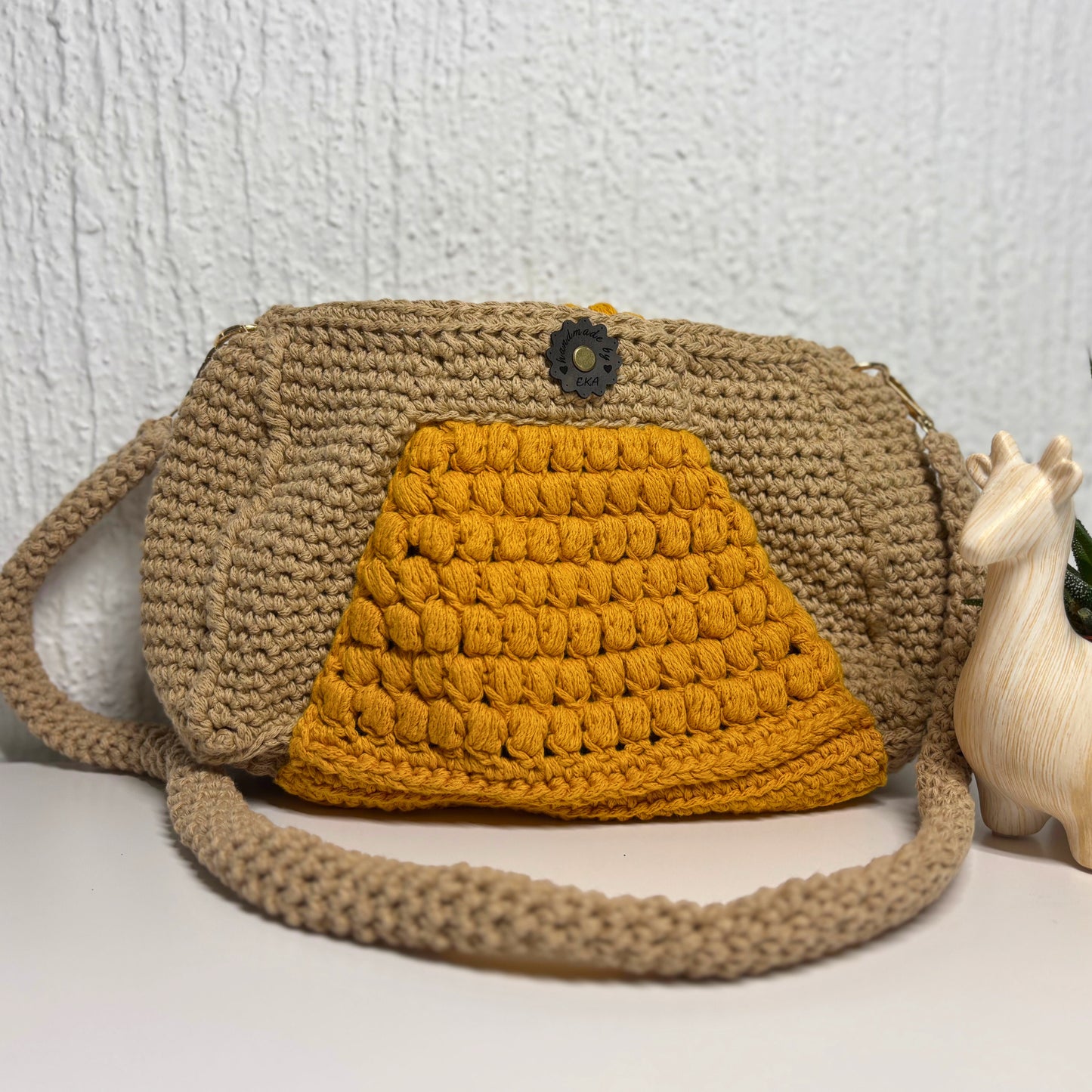 Crocheted bag with a yellow front panel and beige strap on a white background