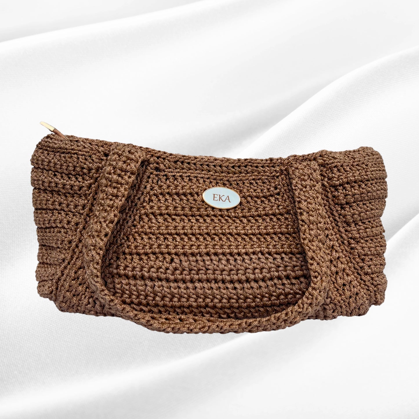Front view of the handcrafted Elena shoulder bag by Eka in metallic bronze-gold crochet, featuring an oval gold logo plaque centered on the woven texture.