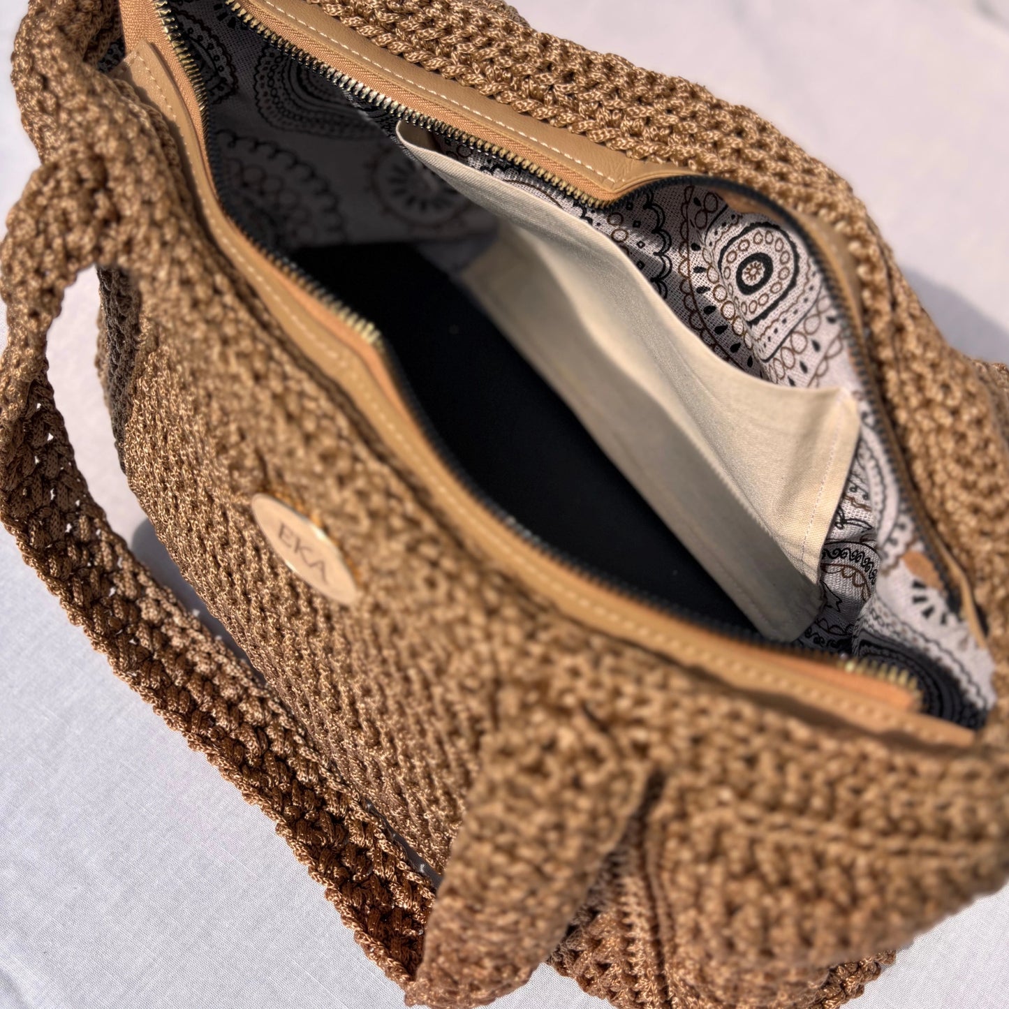 Angled interior view of the Elena bag showing the detailed paisley print lining, slip pocket, and smooth top zipper set in a beige frame.