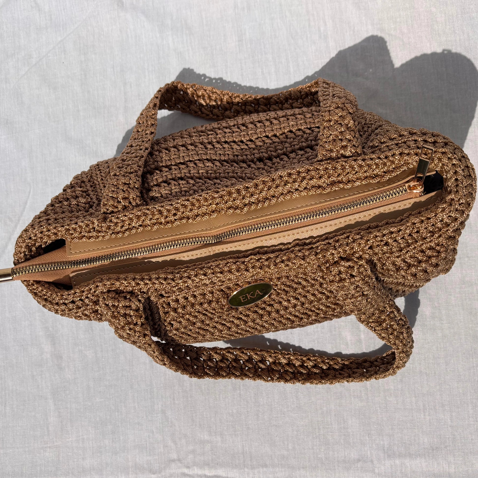 Top-down view of the closed Elena purse showing the zipped beige leatherette trim, integrated wide crochet straps, and oval gold EKA emblem.