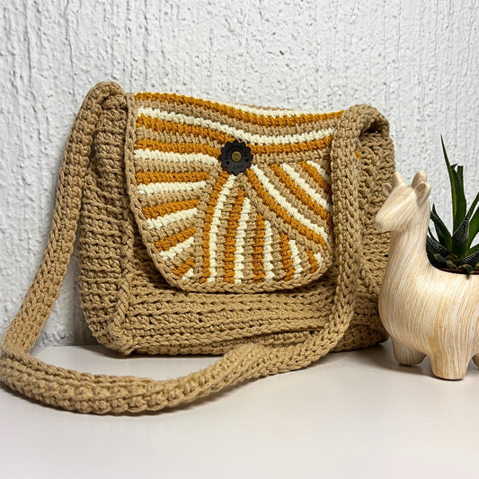 Crocheted bag with a sunburst pattern next to a wooden plant holder on a white surface.