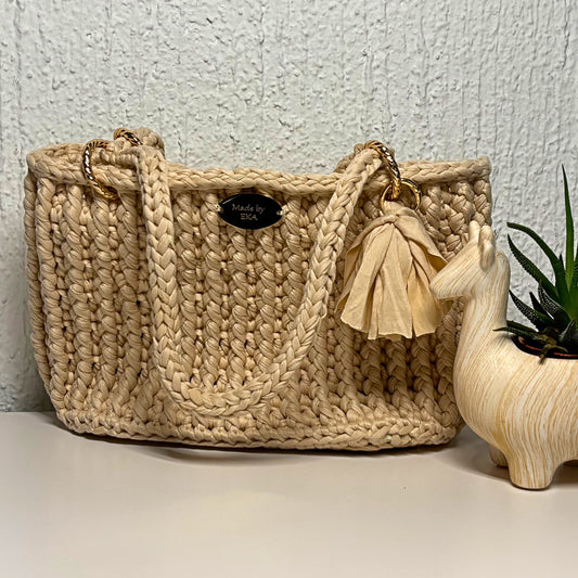 Beige handbag with a tassel on a light surface against a textured wall.