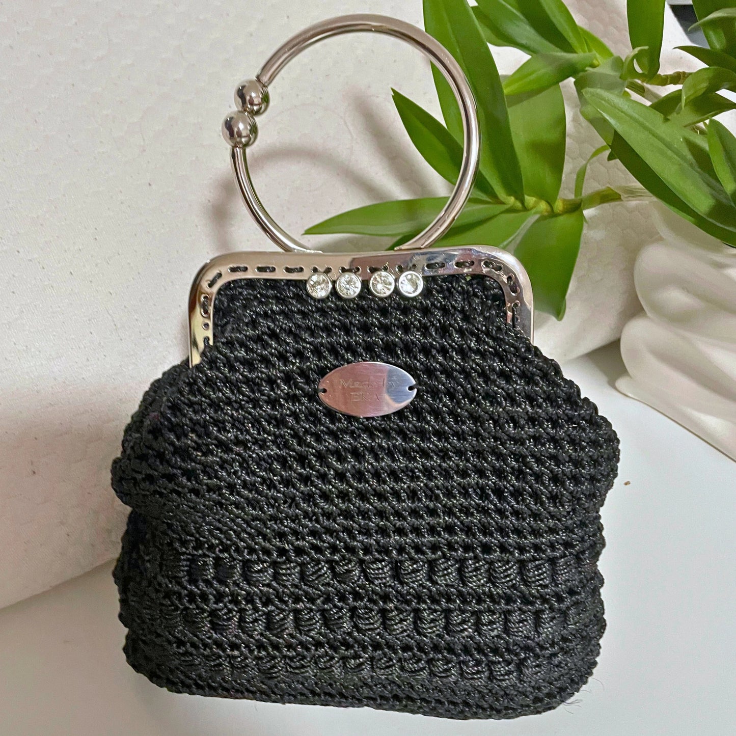 Black woven handbag with a metal handle on a light background