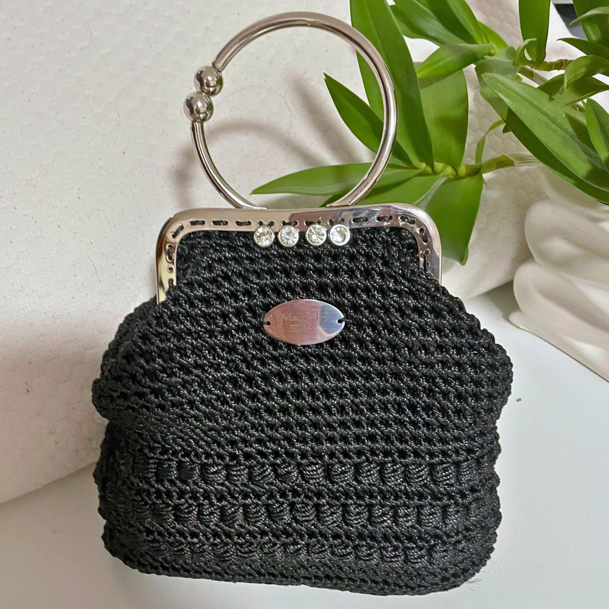 Black woven handbag with a metal handle on a light background
