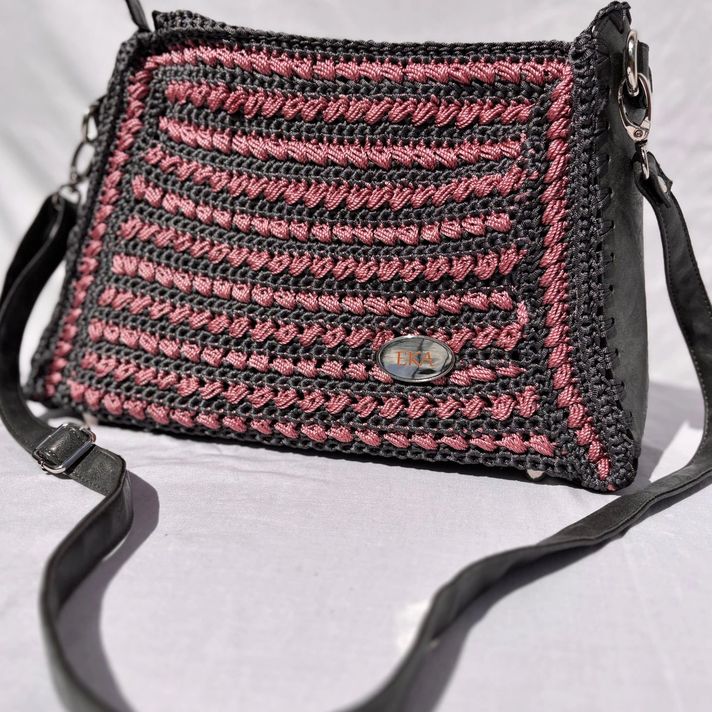 Close-up angled view of the Gloria purse resting on a surface, displaying the detailed horizontal yarn stitching, real leather framing, silver hardware, and oval logo emblem.