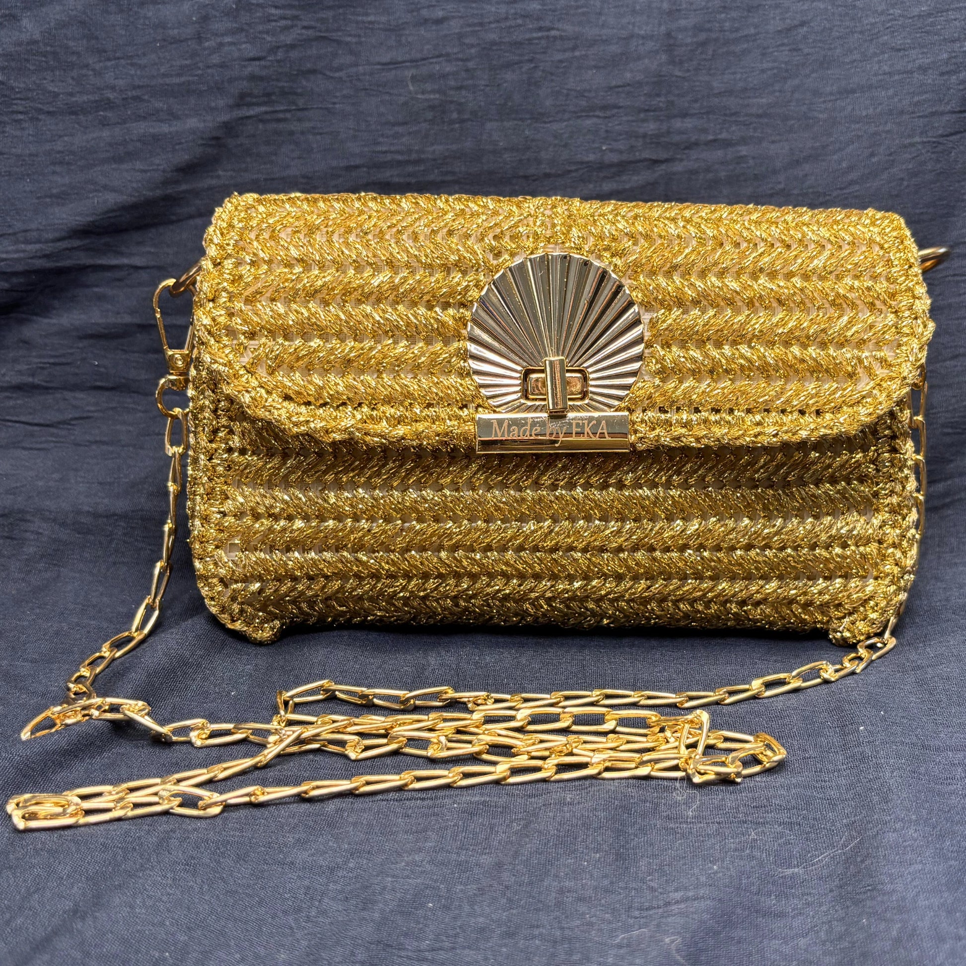 Gold textured handbag with chain strap on a dark blue background