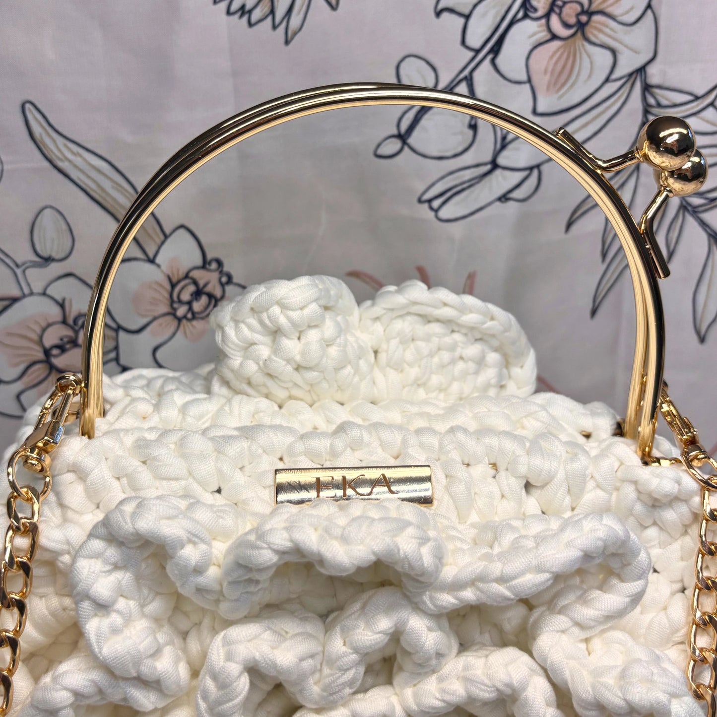 White textured handbag with gold accents on a floral-patterned background