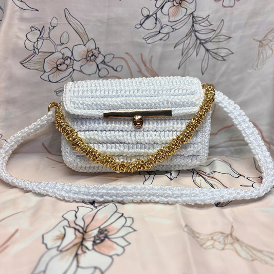 White crochet handbag with gold chain strap on a floral-patterned surface