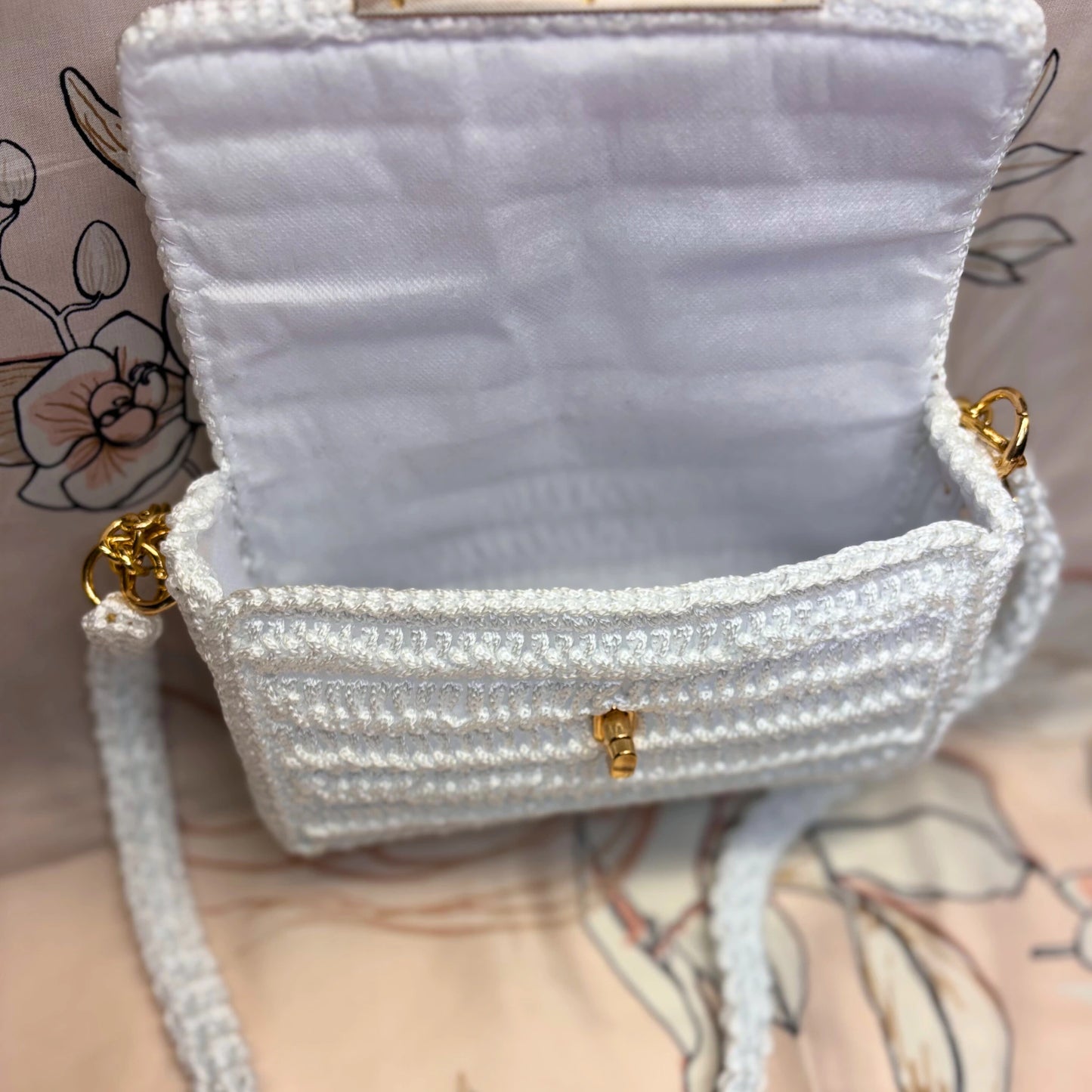 White textured handbag with gold accents on a patterned background